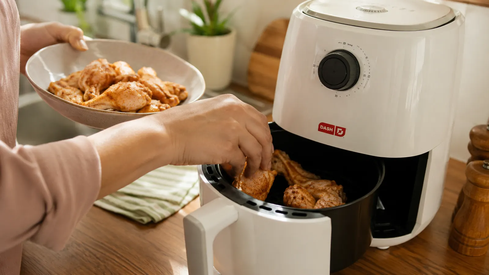 Hand placing a basket of seasoned chicken wings into a small white air fryer