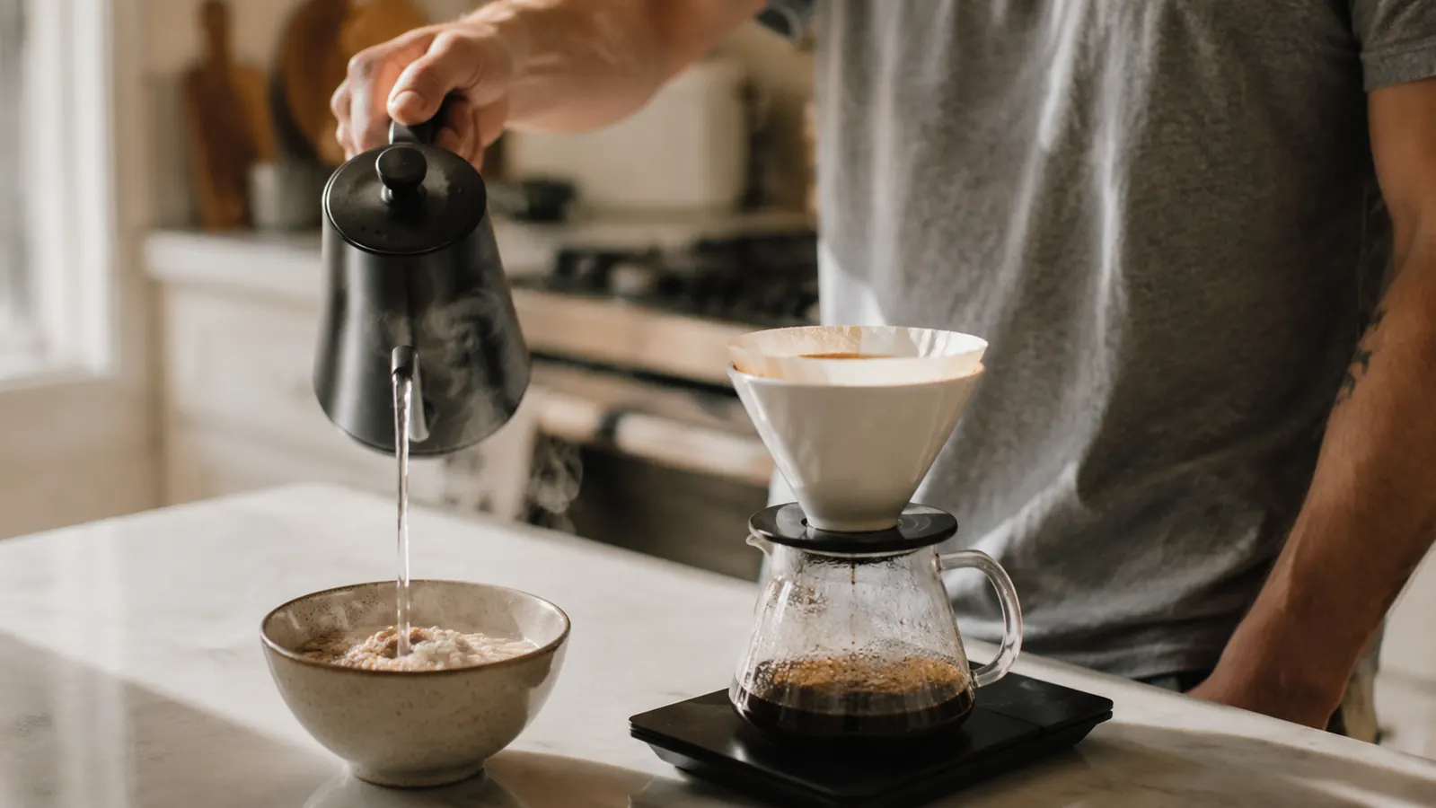 Electric kettle being poured over instant oatmeal and coffee in a small apartment kitchen