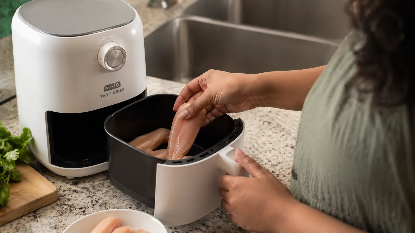 Hand placing chicken tenders in the Dash air fryer basket