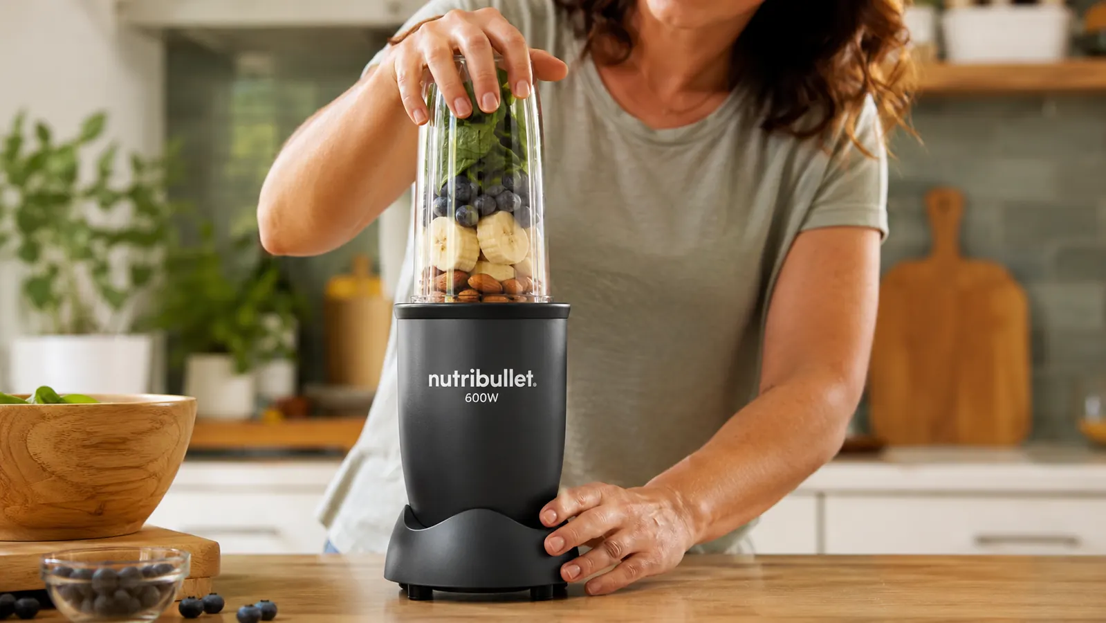 Hand twisting a NutriBullet cup onto the base to blend a smoothie with spinach, banana, and frozen berries