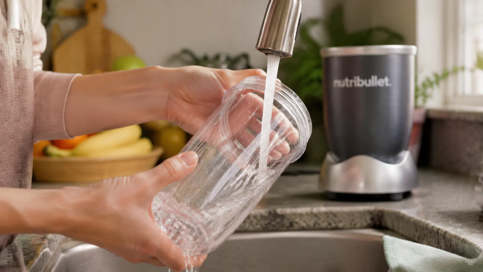 NutriBullet blender cup and blade rinsing under a kitchen faucet, quick and simple cleanup