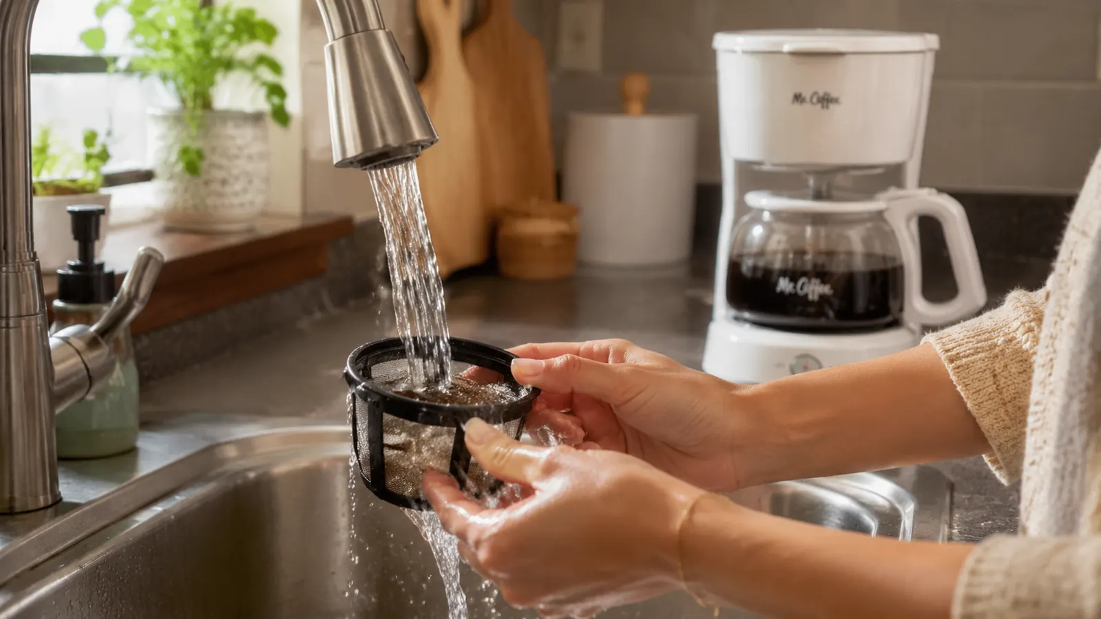 Close-up of the Mr. Coffee 5-Cup Mini reusable filter basket being rinsed under a kitchen faucet after brewing