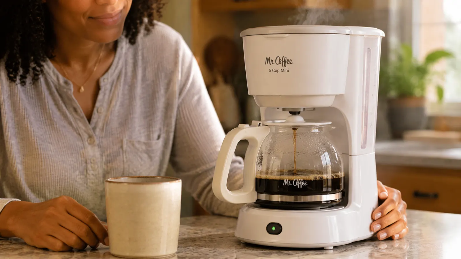 Mr. Coffee 5-Cup Mini on counter with the glass carafe halfway filled with fresh brewed coffee, steam visible